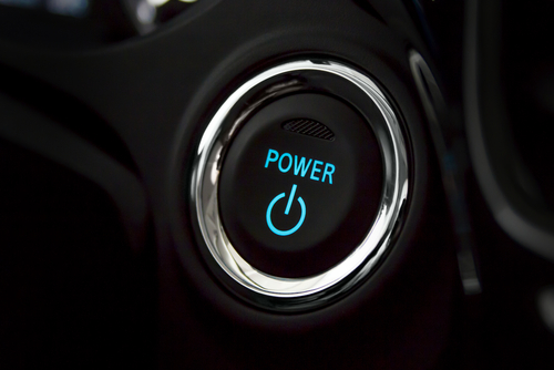 Close-up of a circular power button with a chrome rim. The button is black with the word "POWER" illuminated in blue above a standard power icon, which is also illuminated in blue. The surrounding area appears to be part of a vehicle dashboard.